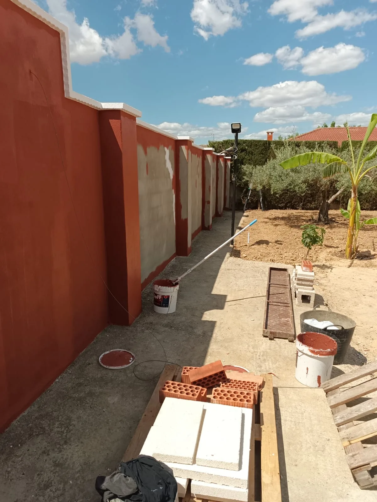 Muro de cerramiento durante el pintado en terracota, junto al jardín